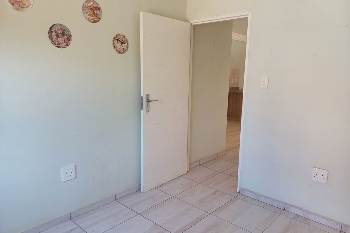 A clean, empty bedroom featuring light-toned tiled flooring, a modern horizontal panel door, and neutral wall finishes, offering a versatile space for customization.