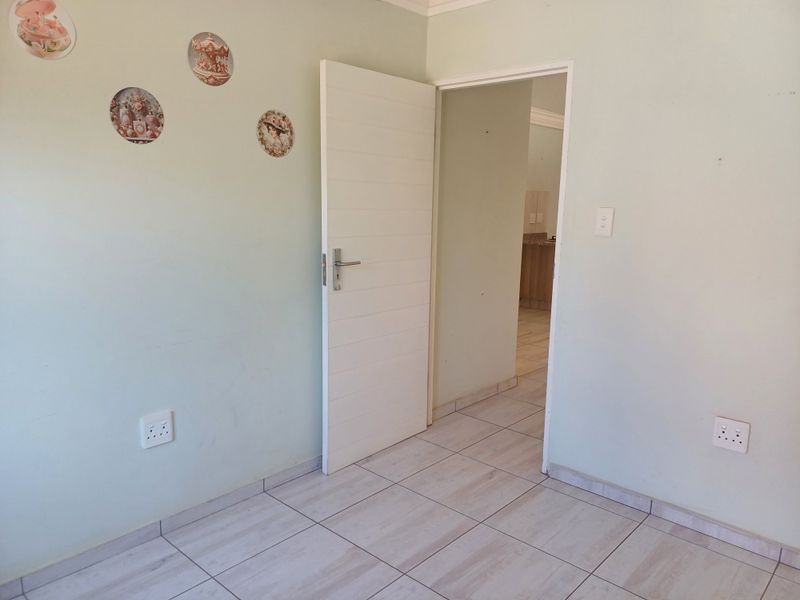 A clean, empty bedroom featuring light-toned tiled flooring, a modern horizontal panel door, and neutral wall finishes, offering a versatile space for customization.