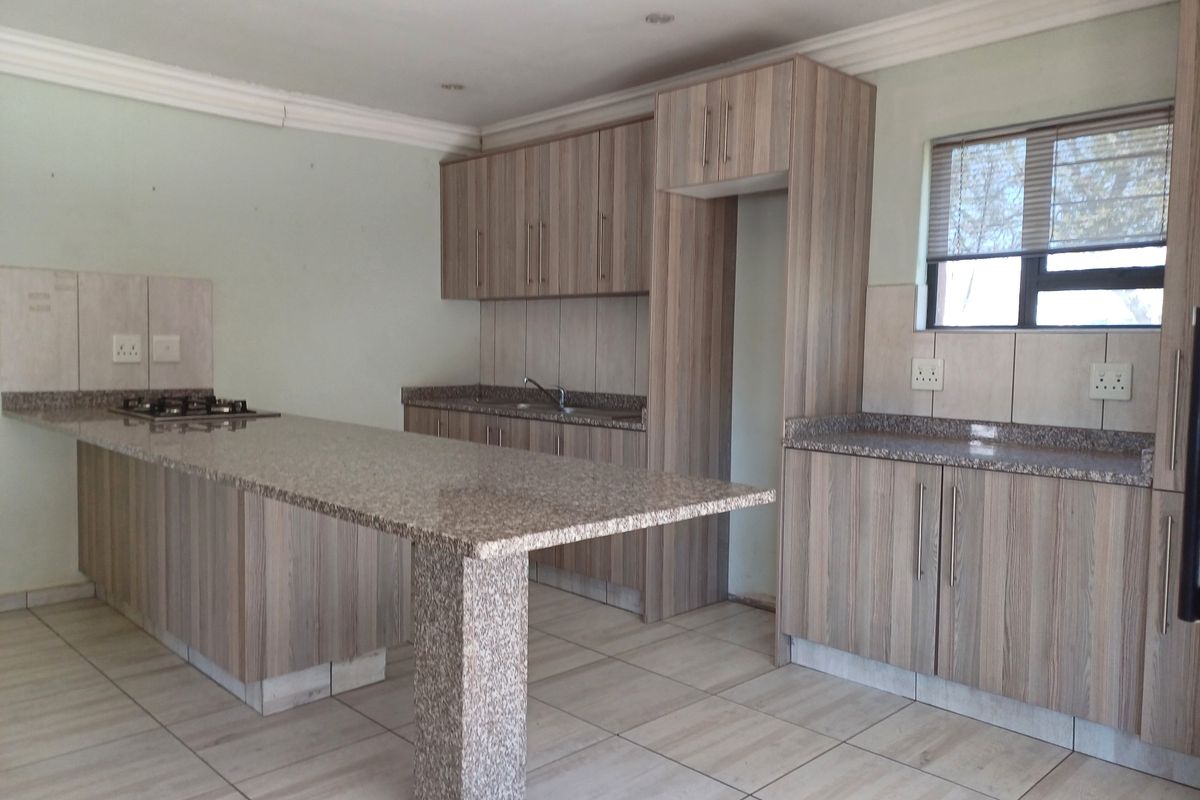 A functional kitchen featuring wood-look cabinetry, granite countertops, a breakfast bar, and a built-in gas hob, presented in a clean, empty space.