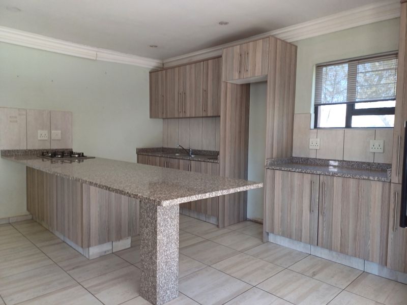 A functional kitchen featuring wood-look cabinetry, granite countertops, a breakfast bar, and a built-in gas hob, presented in a clean, empty space.