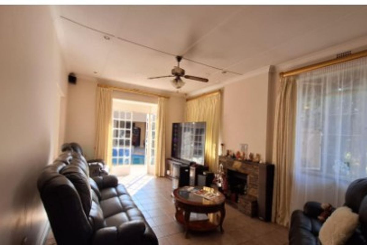 A comfortable living room featuring a stone fireplace, ceiling fan, and French doors that provide direct access to the outdoor pool area.