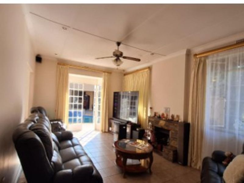 A comfortable living room featuring a stone fireplace, ceiling fan, and French doors that provide direct access to the outdoor pool area.