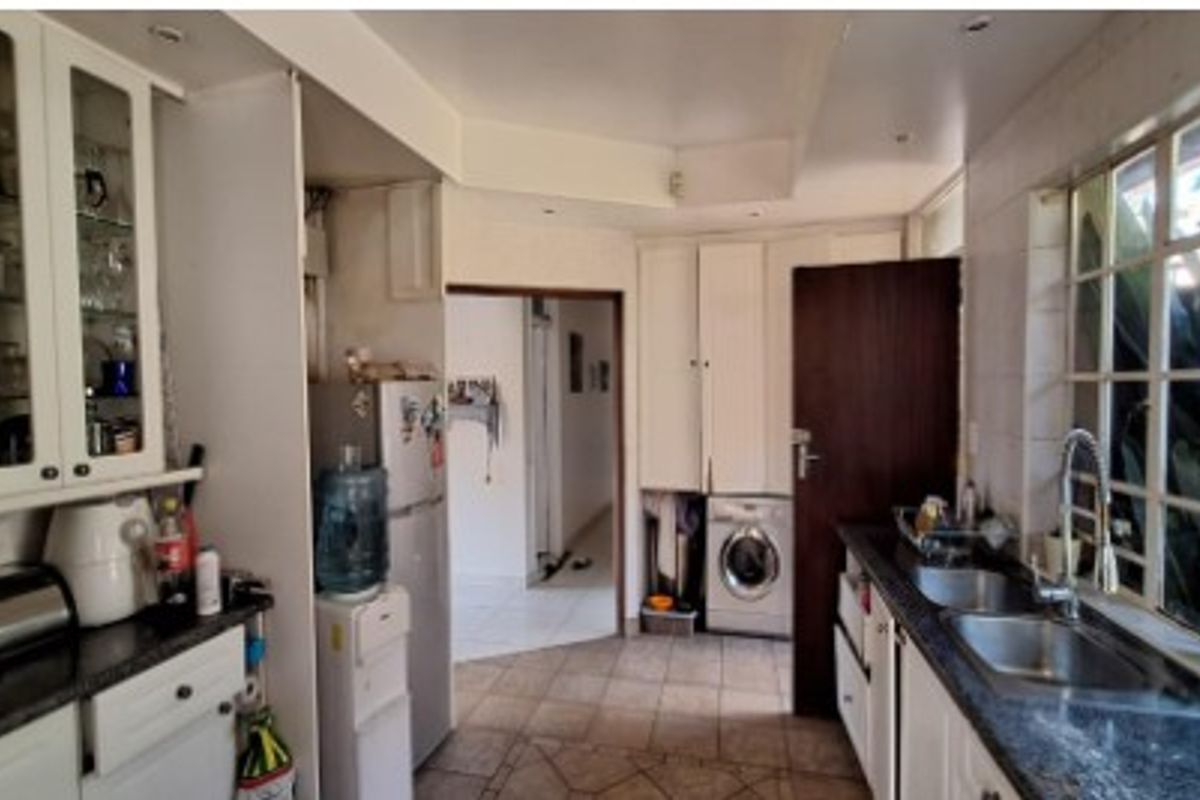A functional kitchen featuring white cabinetry, granite countertops, a double basin sink, and tiled flooring, offering a practical layout with integrated appliance space.
