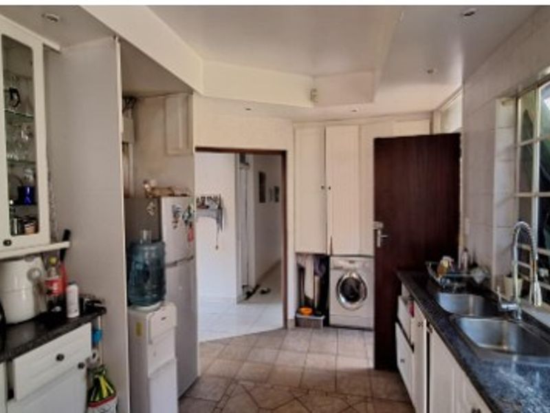 A functional kitchen featuring white cabinetry, granite countertops, a double basin sink, and tiled flooring, offering a practical layout with integrated appliance space.