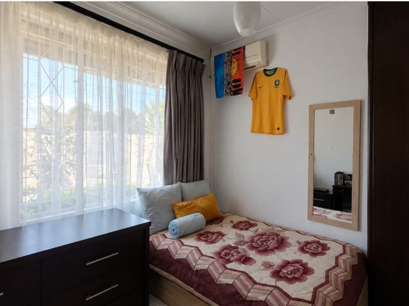 A functional bedroom featuring a built-in wardrobe, split-system air conditioning, and a large window with security bars providing natural light.