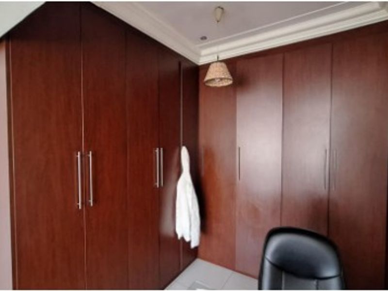A bedroom featuring extensive dark wood built-in cupboards with modern handles and decorative crown molding.