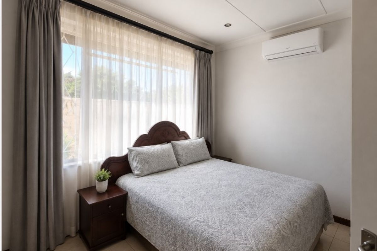 A well-maintained bedroom featuring tiled flooring, recessed ceiling lighting, and a wall-mounted air conditioning unit.