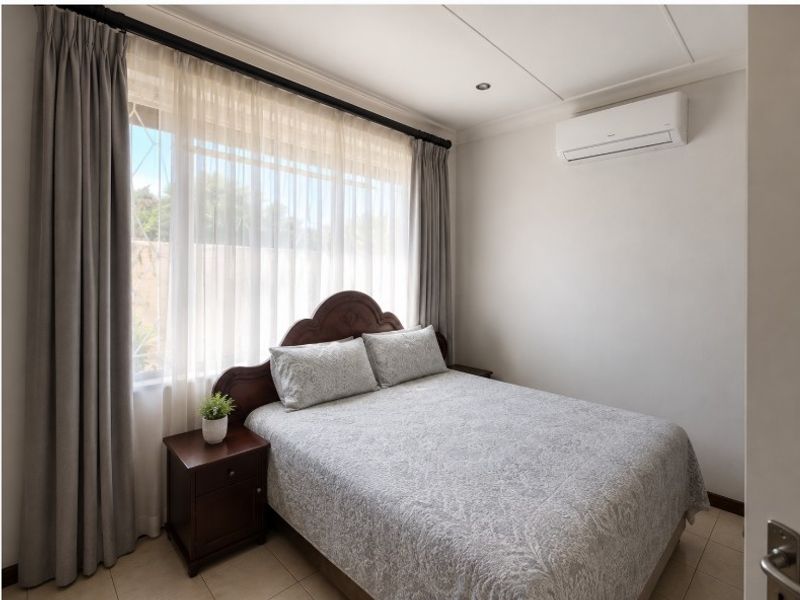 A well-maintained bedroom featuring tiled flooring, recessed ceiling lighting, and a wall-mounted air conditioning unit.