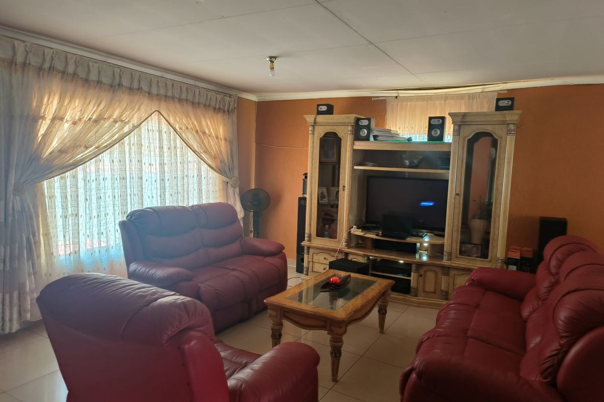 A living room featuring tiled flooring and ceiling panels, currently furnished with a lounge suite and entertainment unit.