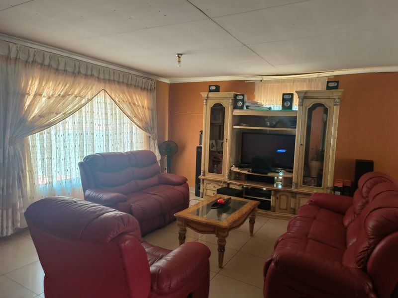 A living room featuring tiled flooring and ceiling panels, currently furnished with a lounge suite and entertainment unit.