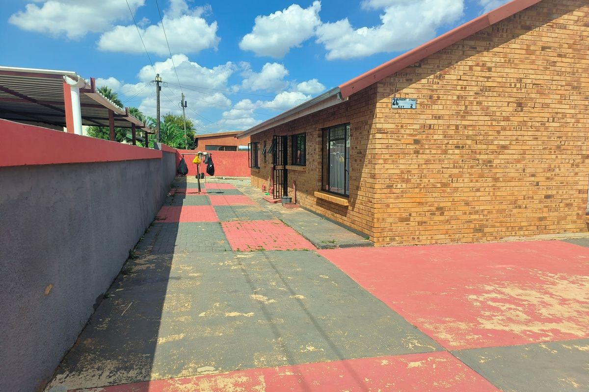 A side view of the property featuring a face brick exterior, paved driveway with worn paint, and a perimeter boundary wall.