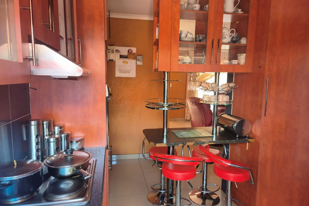 A compact kitchen featuring warm-toned wooden cabinetry, a built-in hob with extractor fan, and a functional breakfast bar area with tiled flooring.