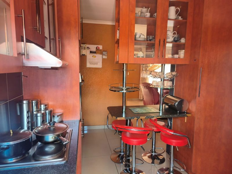 A compact kitchen featuring warm-toned wooden cabinetry, a built-in hob with extractor fan, and a functional breakfast bar area with tiled flooring.