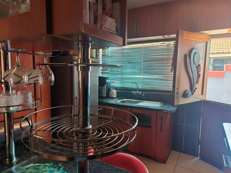 A dated kitchen area featuring wooden cabinetry, a stainless steel sink, and a window with venetian blinds, requiring some maintenance and cosmetic updates.