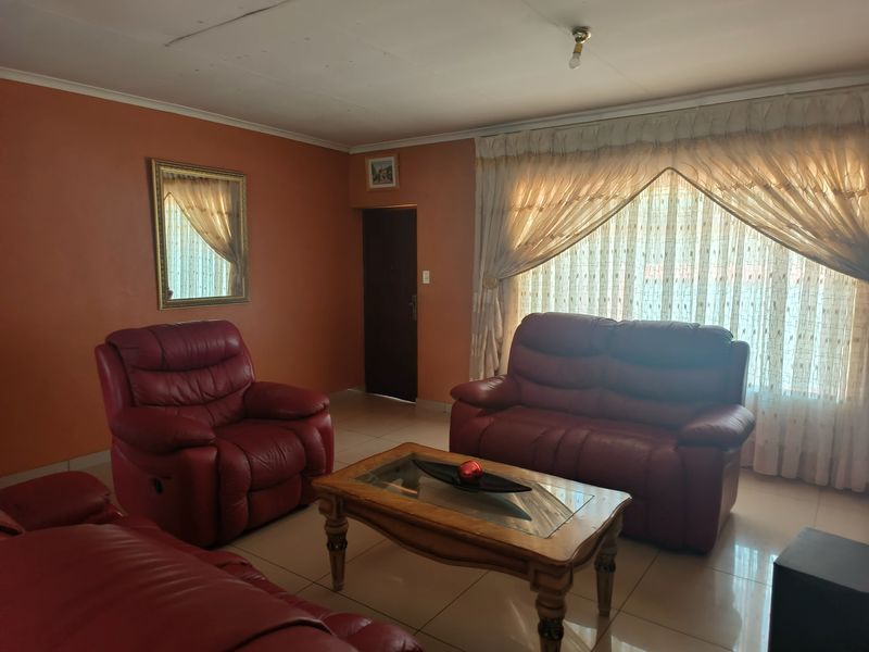 A living room featuring tiled flooring and large windows with curtains, providing a functional space with potential for modern updates.