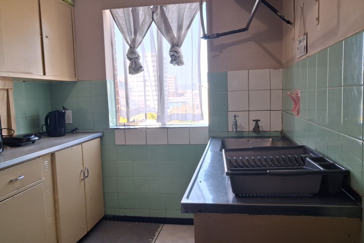 A dated kitchen featuring original cabinetry, a stainless steel sink, and tiled splashbacks, offering potential for a modern renovation.