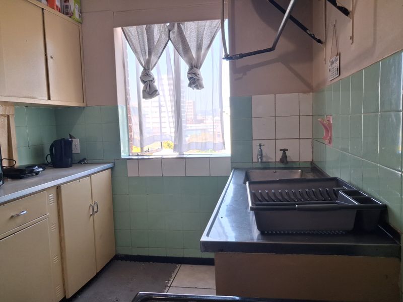 A dated kitchen featuring original cabinetry, a stainless steel sink, and tiled splashbacks, offering potential for a modern renovation.