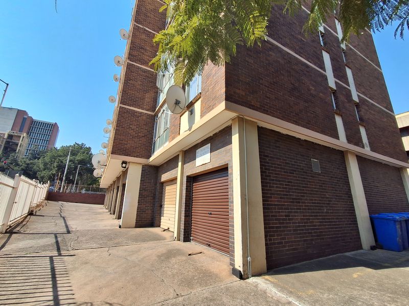 Exterior view of an apartment building featuring a brick facade, concrete driveway, and multiple ground-level roller shutter garage doors.