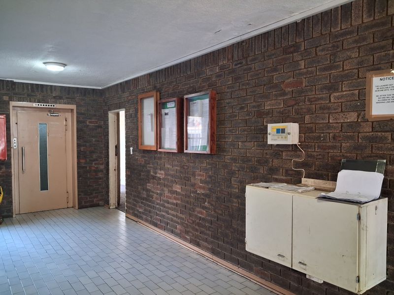 Communal apartment building entrance lobby featuring exposed brick walls, tiled flooring, an elevator, and built-in notice boards.