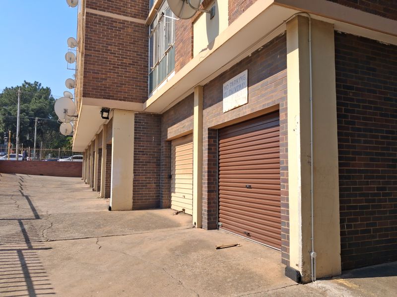 Exterior view of the apartment complex showing a row of secure roller shutter garage doors and a concrete driveway.