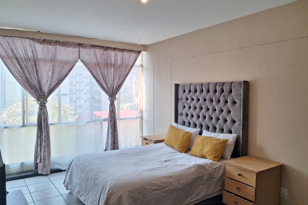 A bedroom featuring tiled flooring and a large floor-to-ceiling window that provides ample natural light.