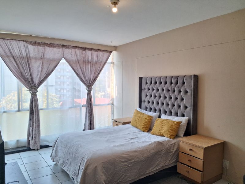 A bedroom featuring tiled flooring and a large floor-to-ceiling window that provides ample natural light.