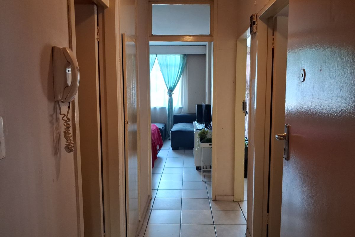 A functional apartment hallway featuring tiled flooring, an intercom system, and access to adjacent rooms, showing signs of wear and dated finishes.