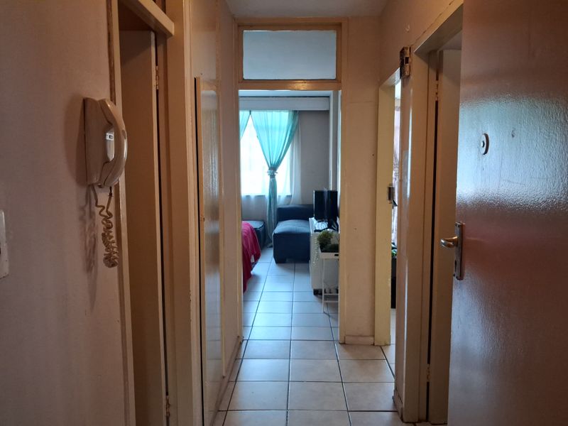 A functional apartment hallway featuring tiled flooring, an intercom system, and access to adjacent rooms, showing signs of wear and dated finishes.