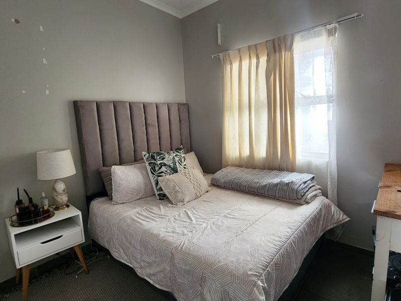 A compact bedroom featuring neutral wall tones, a window with curtain rod, and tiled flooring.