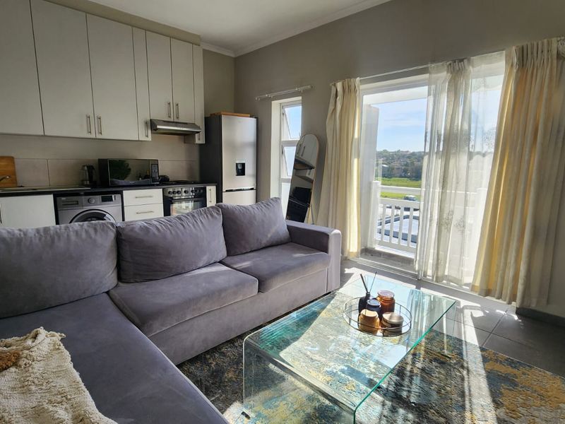 Open-plan living area featuring a modern kitchen with built-in cabinetry and appliances, leading to a balcony with natural light.