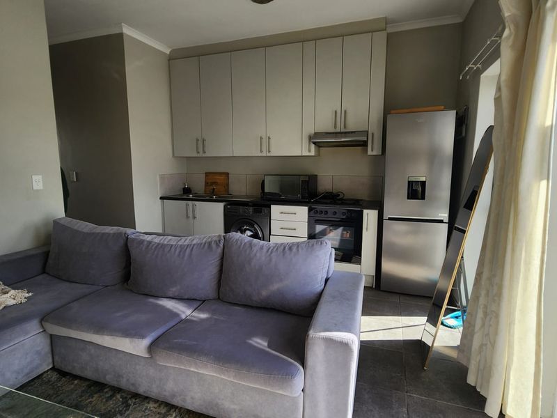 Open-plan living area featuring a compact kitchen with built-in cabinetry, integrated appliances, and direct access to an outdoor balcony through a sliding door.