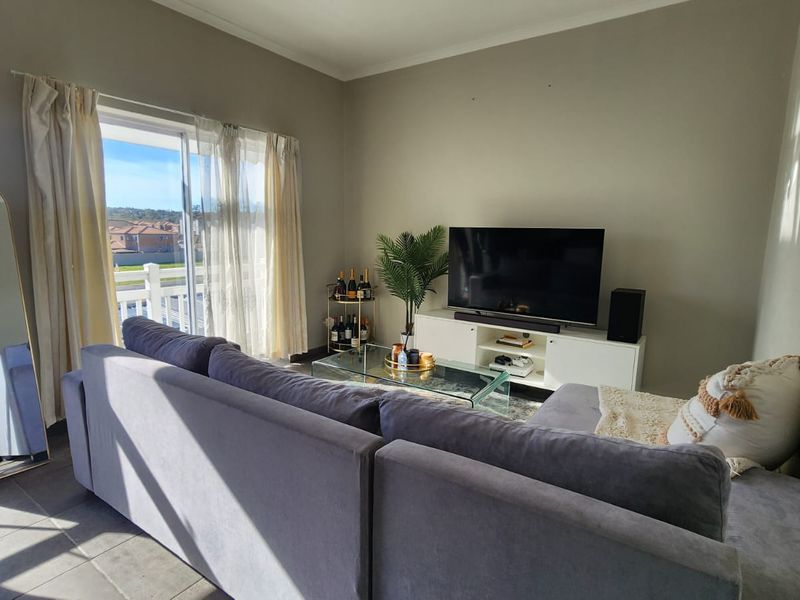 A comfortable living room featuring tiled flooring and a large sliding glass door that provides access to an outdoor balcony area.