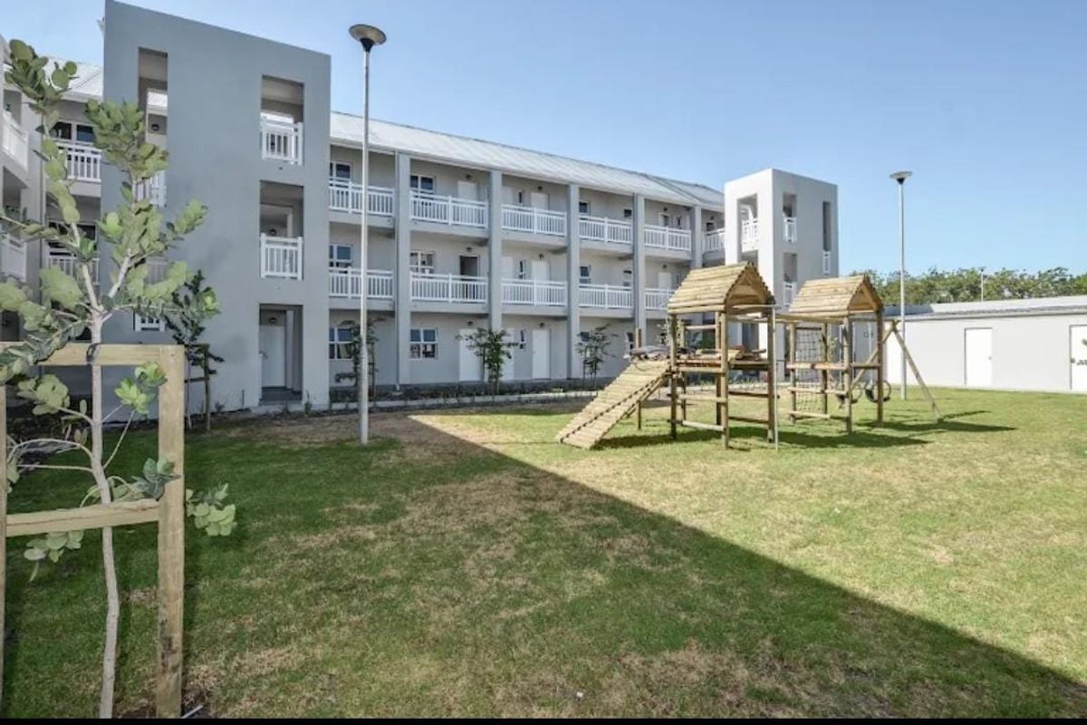 A view of the rear exterior of a multi-story apartment building featuring balconies and a shared lawn area with a playground.