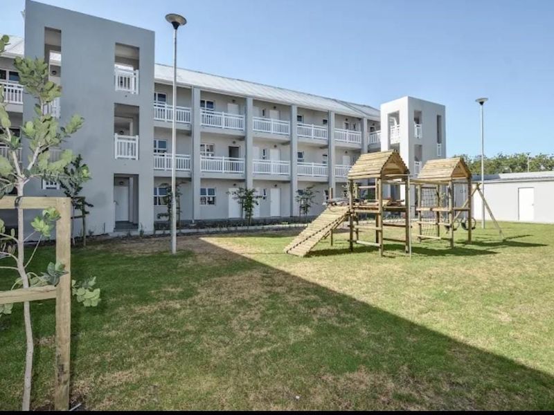A view of the rear exterior of a multi-story apartment building featuring balconies and a shared lawn area with a playground.
