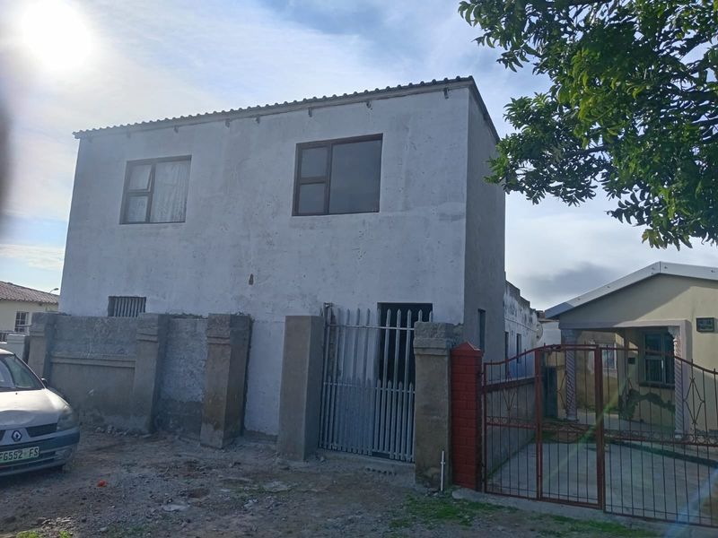Front elevation of a two-story residential property featuring unfinished plaster walls, metal security gates, and concrete boundary fencing.
