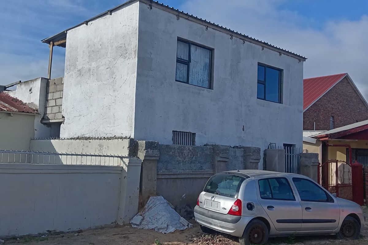 A two-story residential building featuring an unfinished exterior facade, aluminium window frames, and a perimeter wall with security spikes.