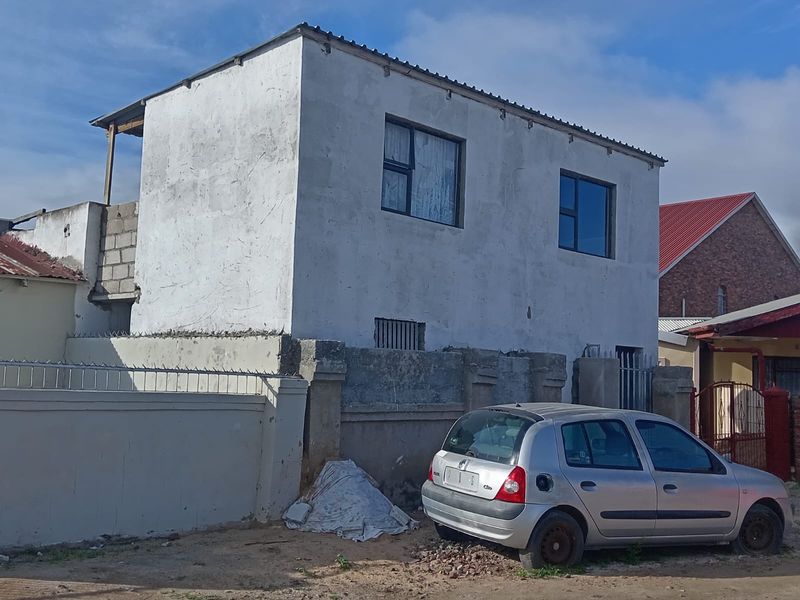 A two-story residential building featuring an unfinished exterior facade, aluminium window frames, and a perimeter wall with security spikes.