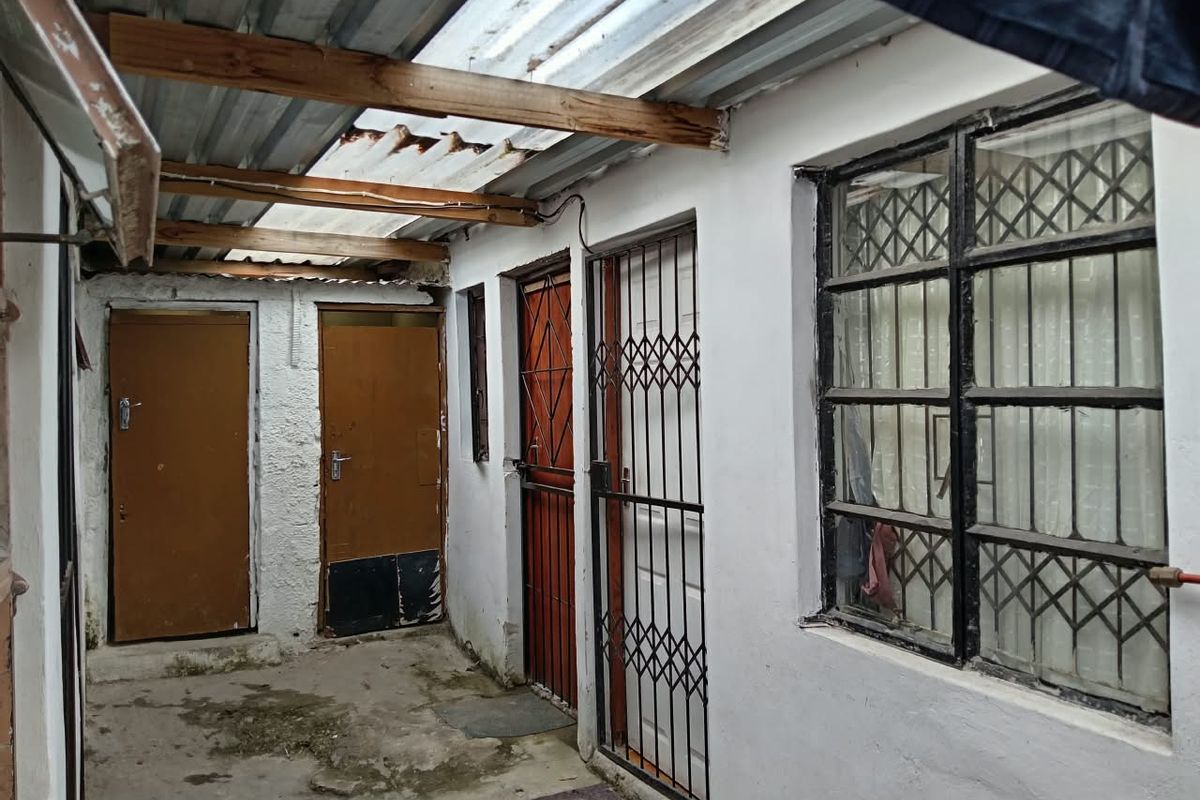 A covered outdoor patio area featuring concrete flooring, security gates, and multiple access doors, requiring maintenance and cosmetic updates.