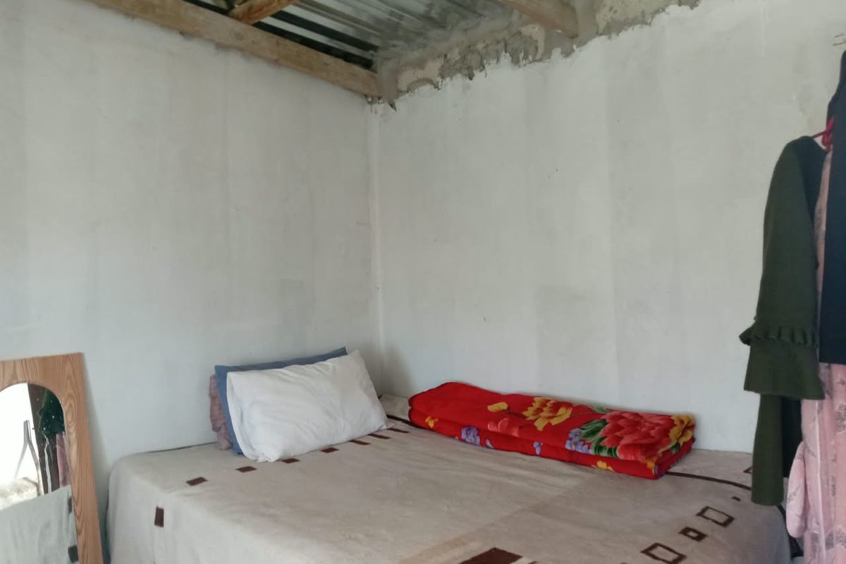 A bedroom featuring unfinished walls and exposed timber rafters with corrugated metal roofing, requiring significant interior finishing and ceiling installation.