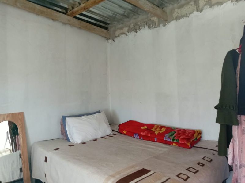 A bedroom featuring unfinished walls and exposed timber rafters with corrugated metal roofing, requiring significant interior finishing and ceiling installation.