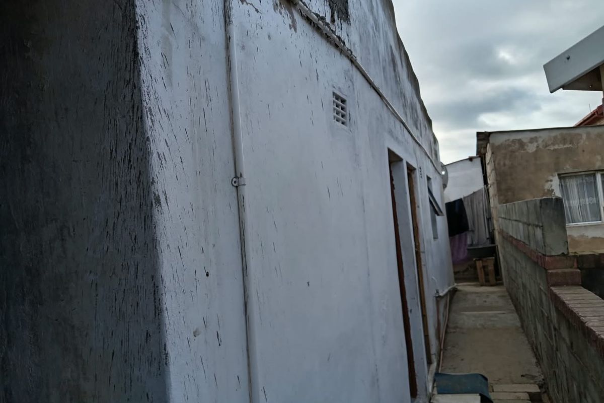 Side view of the property showing exterior wall with visible weathering, staining, and basic boundary wall infrastructure.