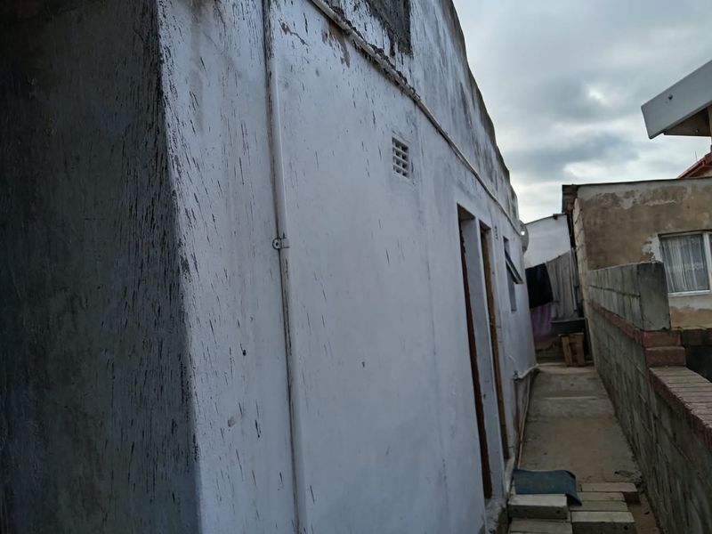 Side view of the property showing exterior wall with visible weathering, staining, and basic boundary wall infrastructure.