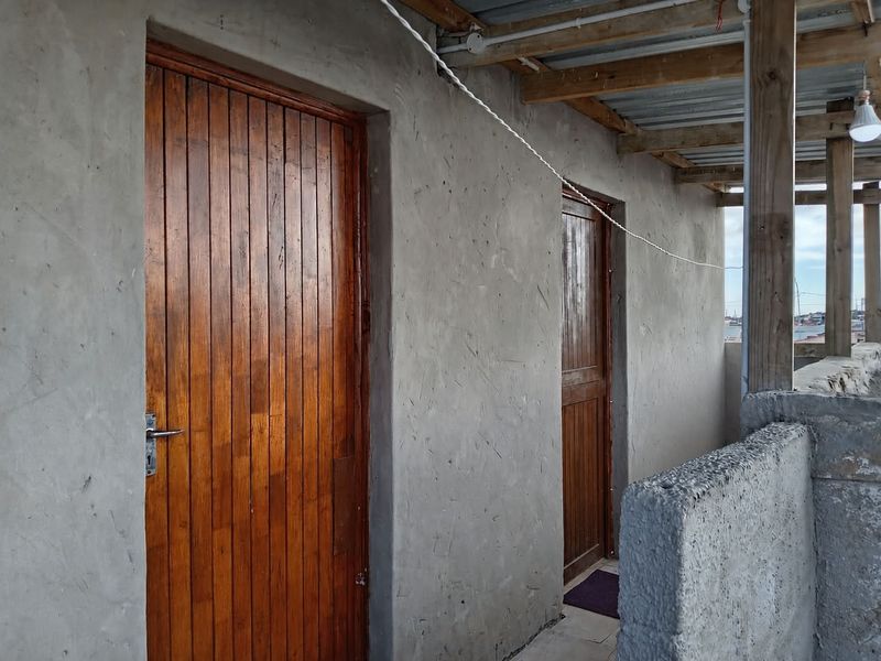 A covered outdoor balcony area featuring timber doors and unfinished concrete walls, providing access to the property's exterior spaces.