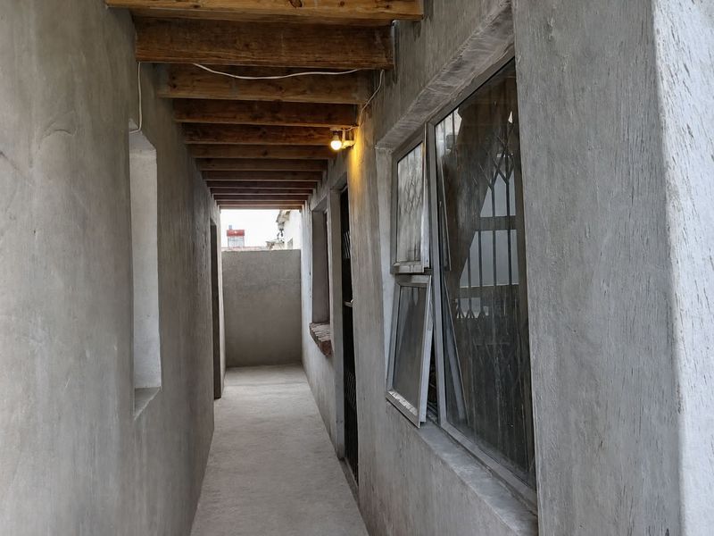 A narrow, unfinished exterior-style hallway featuring exposed timber ceiling beams, concrete walls, and security-fitted windows.