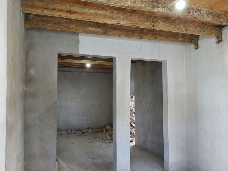 An unfinished interior space featuring exposed timber ceiling beams, raw cement walls, and concrete flooring, currently in a shell construction state.