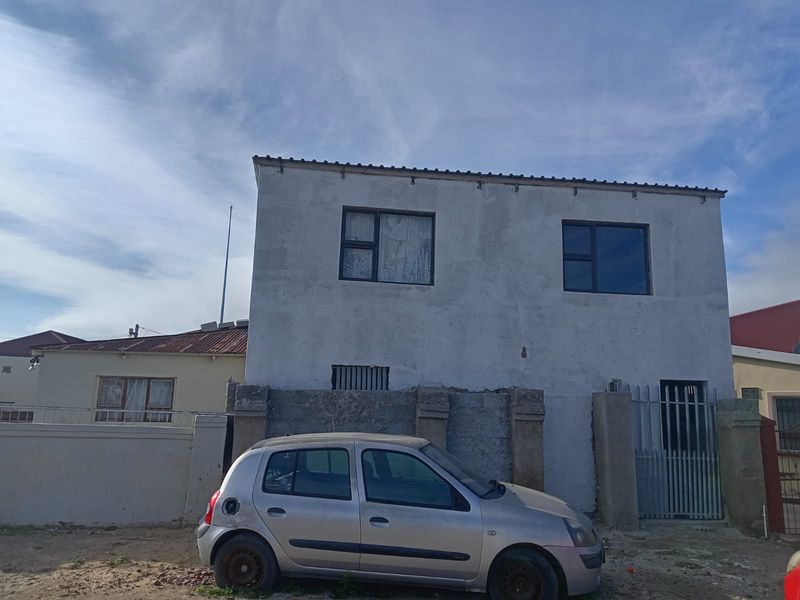 Front elevation of a two-story residential property featuring an unfinished concrete facade, aluminium window frames, and a secure gated entrance.