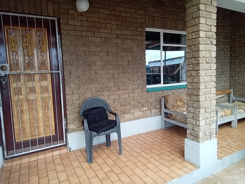A covered patio area featuring brick wall finishes, tiled flooring, and secure access points with security gates and window bars.