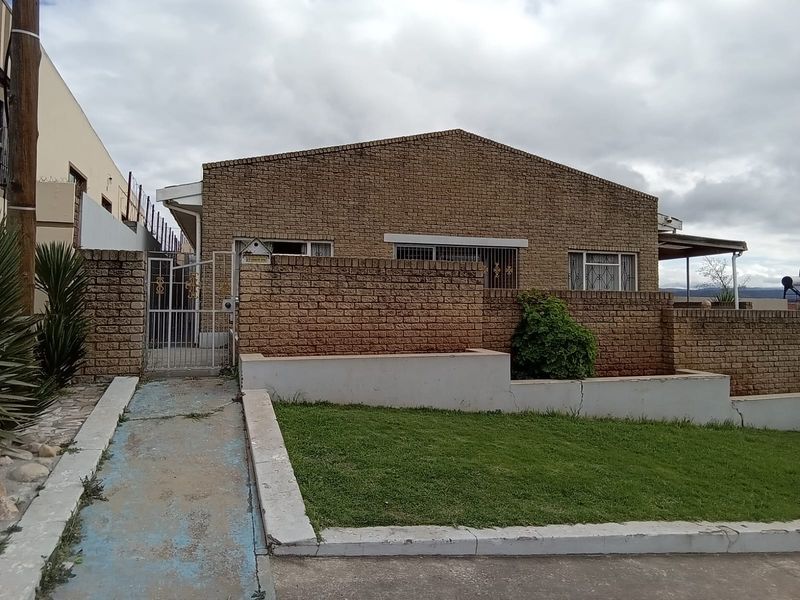 Front view of a face brick house featuring a security gate, security bars on windows, and a small front garden with a retaining wall.