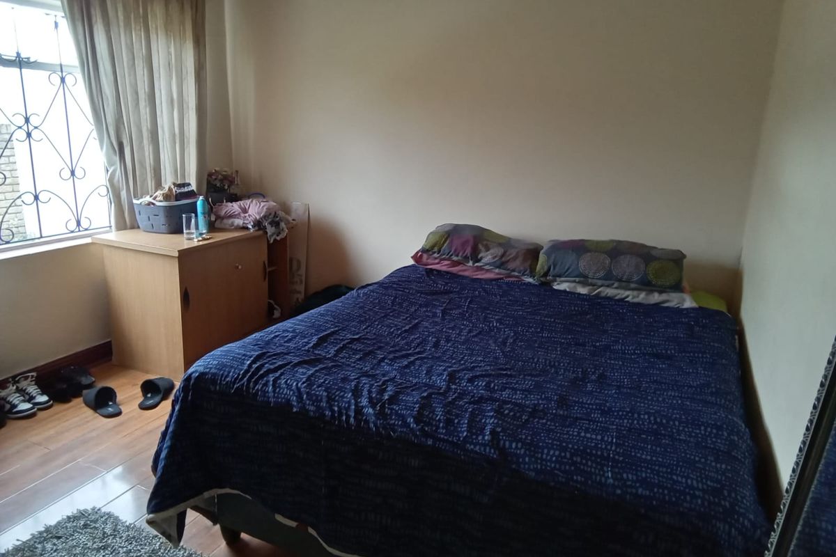 A standard bedroom featuring laminate flooring, a window with security bars, and curtain rails.