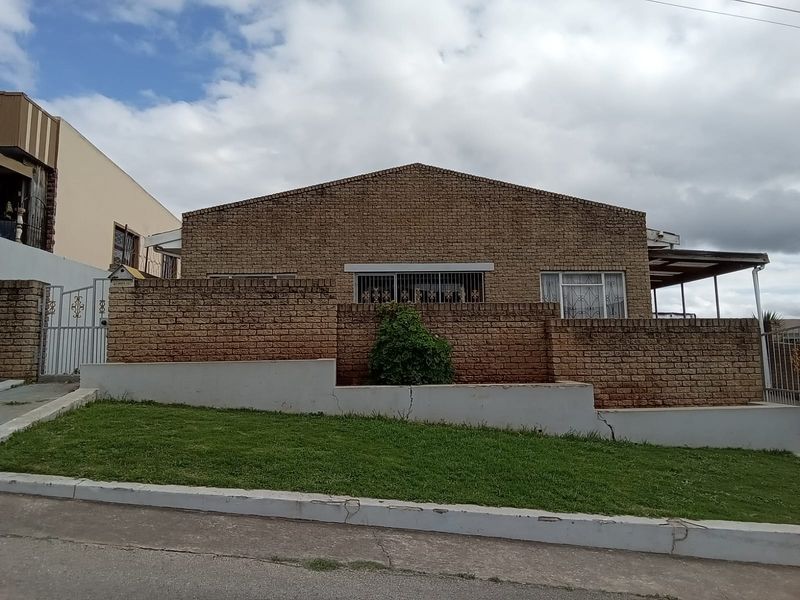 Front view of a face brick house featuring a low boundary wall, security bars on windows, and a small front lawn area.